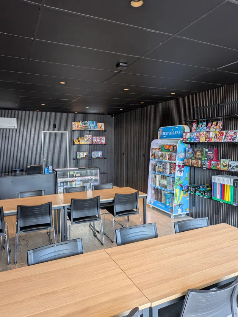 Inside Lootable: rows of wooden tables and black chairs, with board games and card games on the shelves and the display cabinet by the counter
